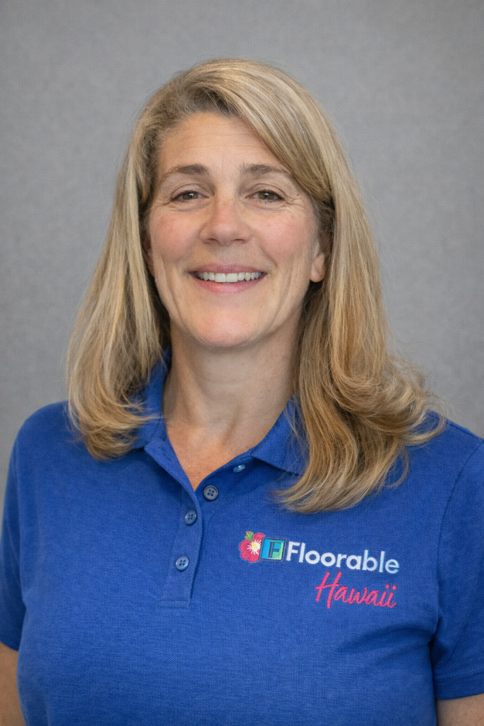 Professional headshot of a woman in a blue branded shirt with "Floorable Hawaii" logo, smiling against a neutral background, representing the expert team in flooring solutions.