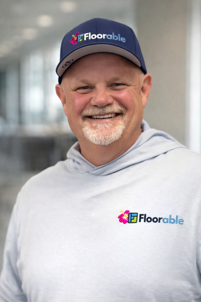 Man smiling in a gray hoodie and blue cap with "Floorable" logo, representing the expert flooring team at Floorable Hawaii.