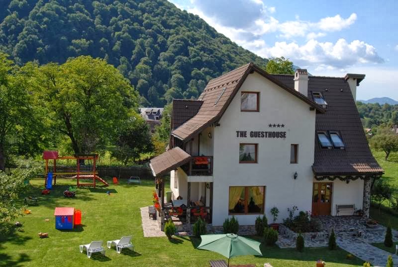 Clădirea "The Guesthouse" din Bran, cu peisaj montan și grădină verde, ideală pentru cazare.