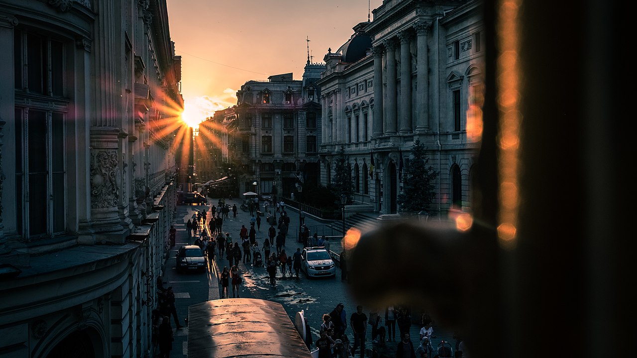 Apus de soare peste străzile istorice ale Centrului Vechi din București, pline de oameni.