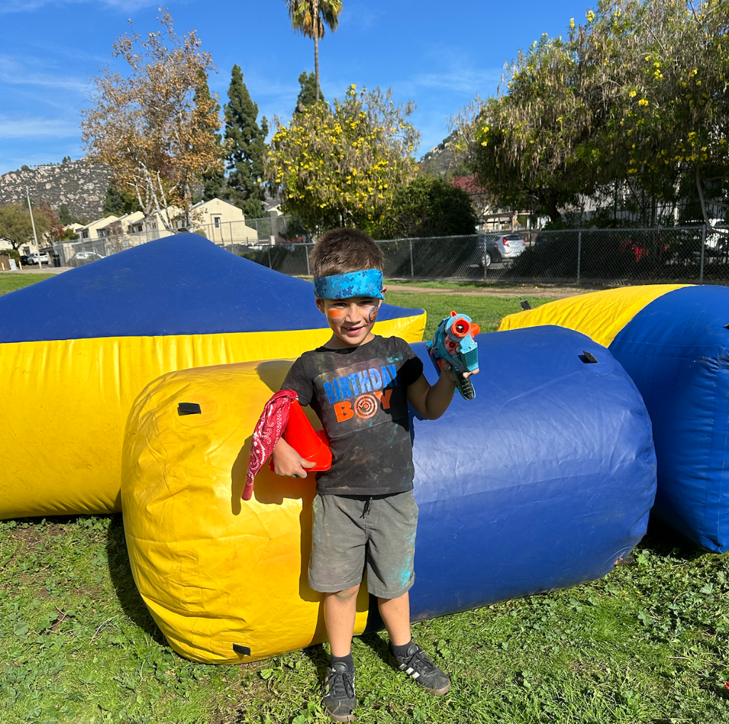 Birthday boy with nerf guns and inflatable barriers - child posing with premium nerf blasters at outdoor party rental