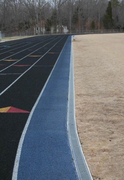 Running track edge detail with concrete curb and drainage channel installation