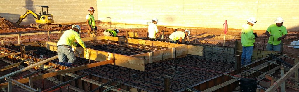 Construction crew forming rebar and pouring concrete foundation for commercial building