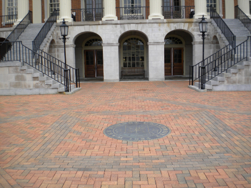 Paver installation with decorative compass rose design, stone steps, and wrought iron railings at building entrance
