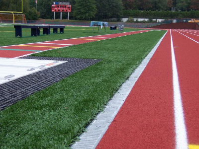 Athletic track edge with turf field and concrete drainage detail