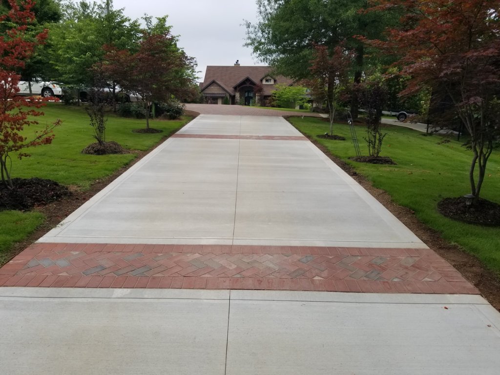 Residential concrete driveway with decorative herringbone paver apron and brick border