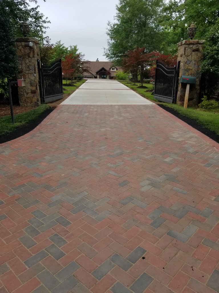 Custom residential driveway with herringbone paver entry, stone pillars, and wrought iron gate