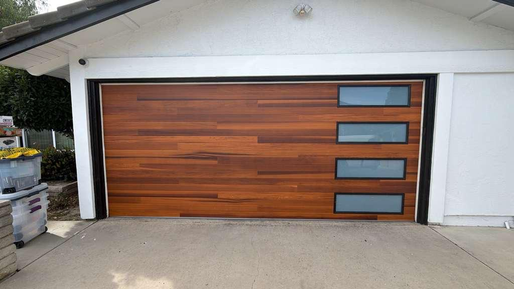 Custom modern wood garage door installation with horizontal slat design and four vertical glass panel windows in Los Angeles residential property