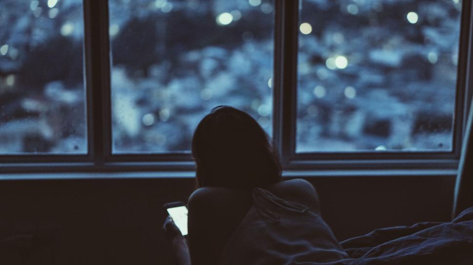 Person sitting on bed looking out window at night