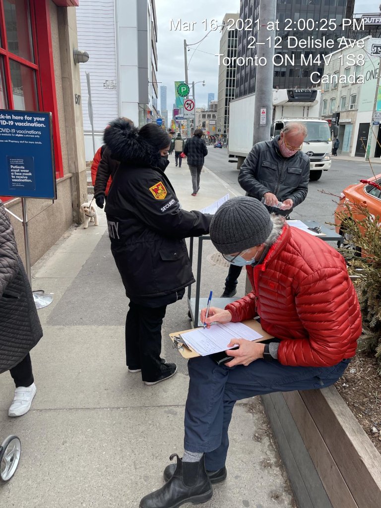 Security personnel assisting individuals in a vaccination line, ensuring safety and order at a public health event in Toronto.