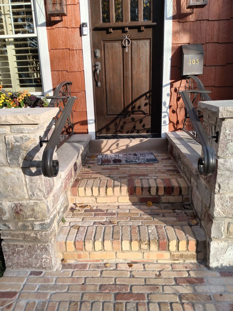 Custom iron front entry step railings with decorative scroll ends installed on brick steps at a residential home in the Fox Valley area.