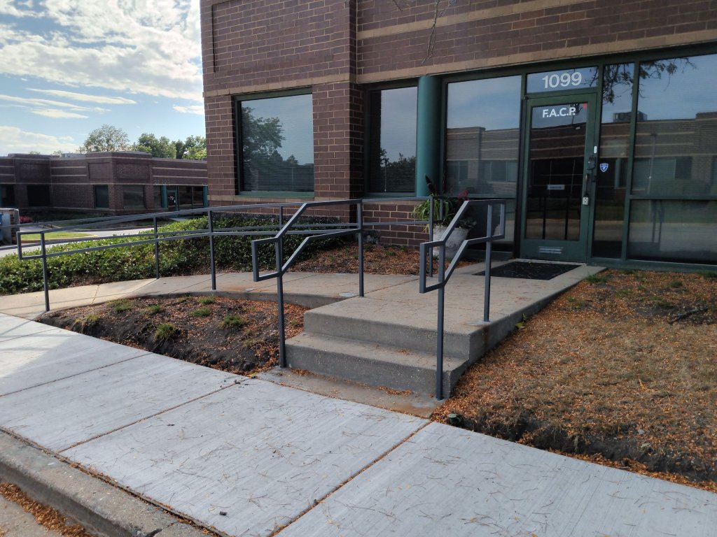 Gray metal commercial stair handrails installed at office building front entrance steps.