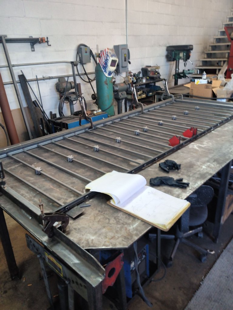 Custom iron railing panel clamped and tack-welded on fabrication table in FOX Welding shop with welding equipment and drill press in background