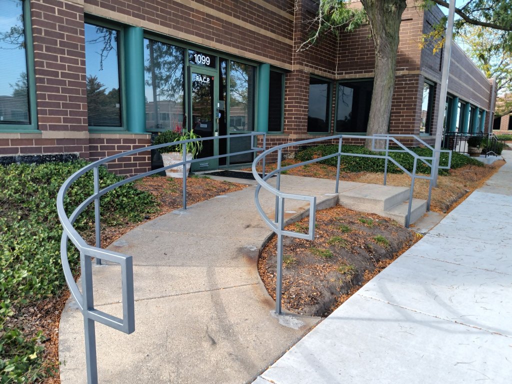 Gray metal ramp and stair handrail system installed at commercial office building entrance.