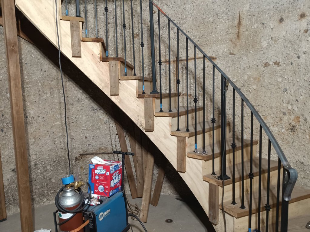 Completed section of custom curved iron stair railing with decorative knuckle balusters installed on wood-tread staircase inside silo tower