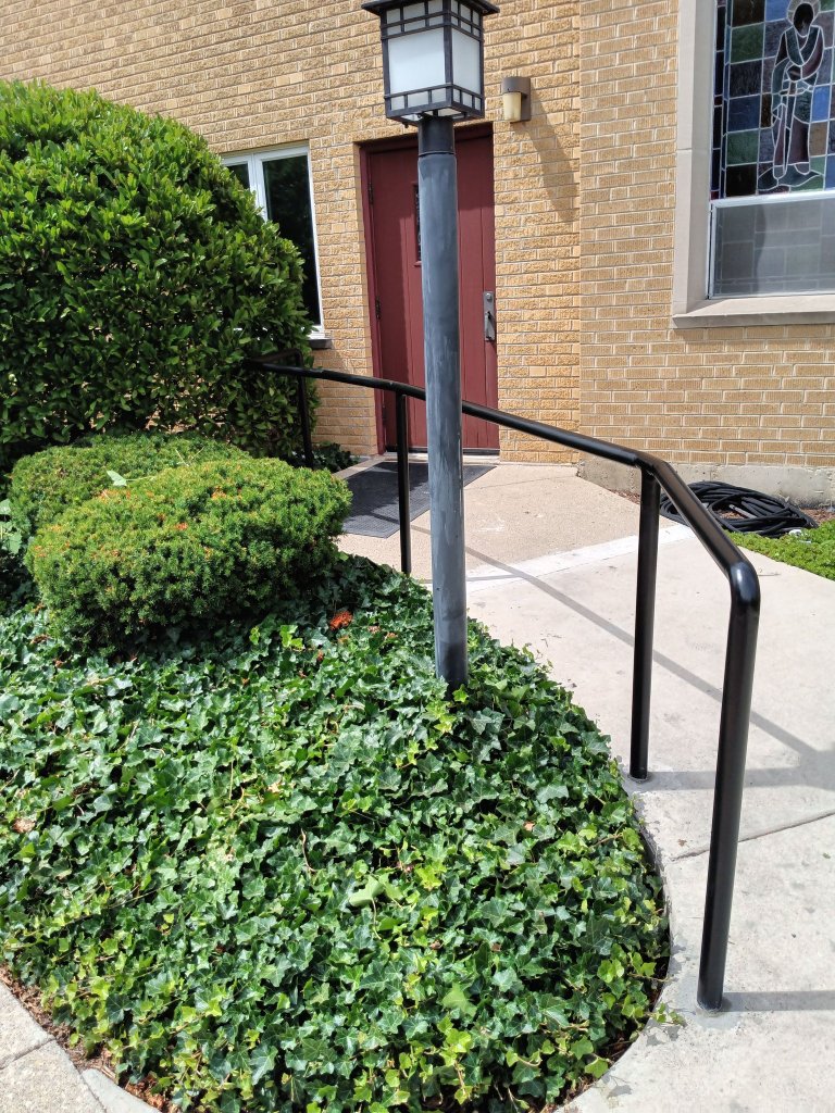 Black iron ramp and stair handrails installed at institutional building entrance with stained glass windows, Fox Valley area IL