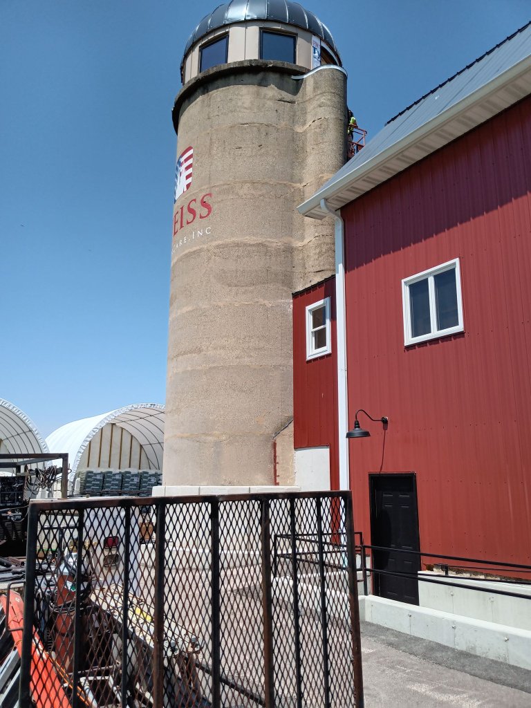 Exterior view of converted silo tower at the property with custom fabricated steel mesh gate panel and red barn structure, IL