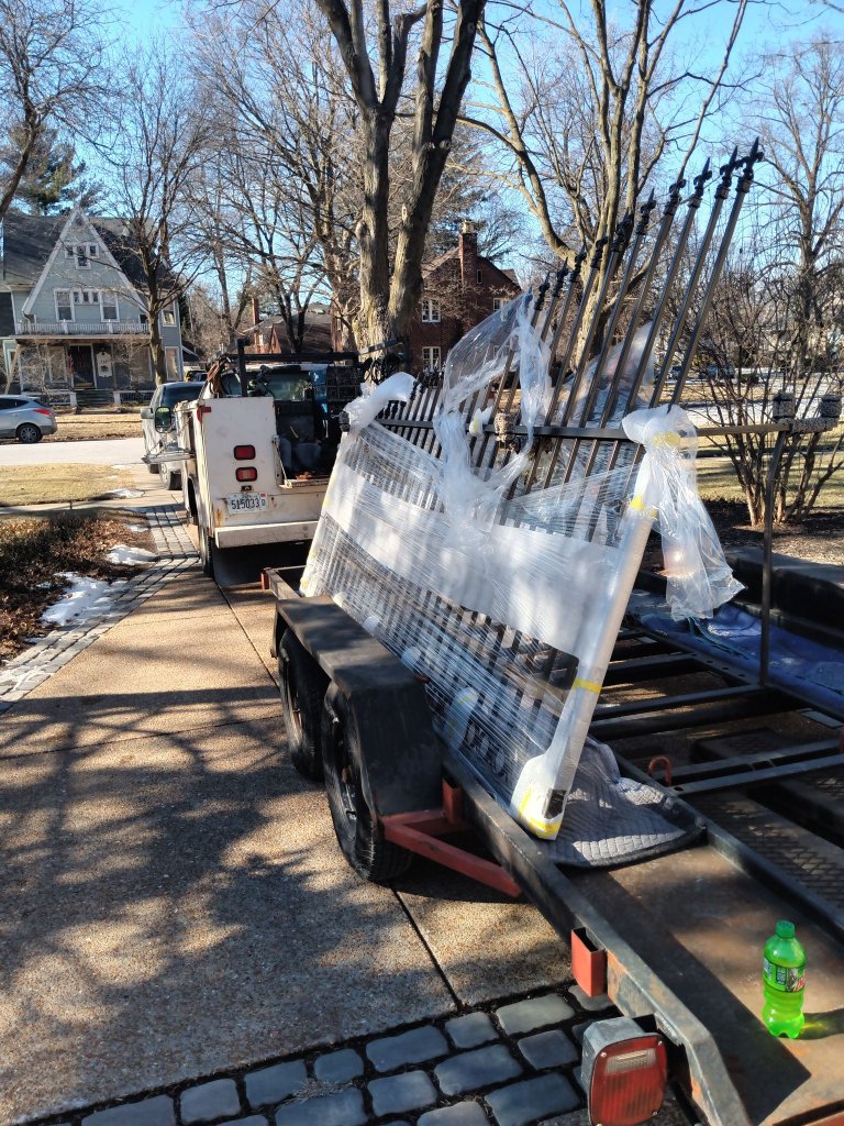 Completed custom ornamental iron fence panels and spear-top gate sections wrapped and transported on trailer to residential job site for installation