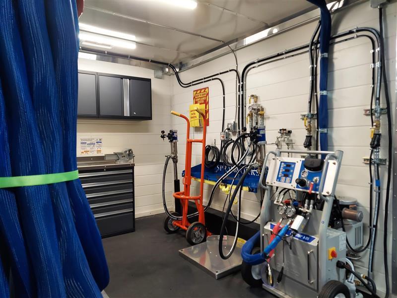Spray foam rig interior workspace showing proportioner, chemical drums, and spray system layout