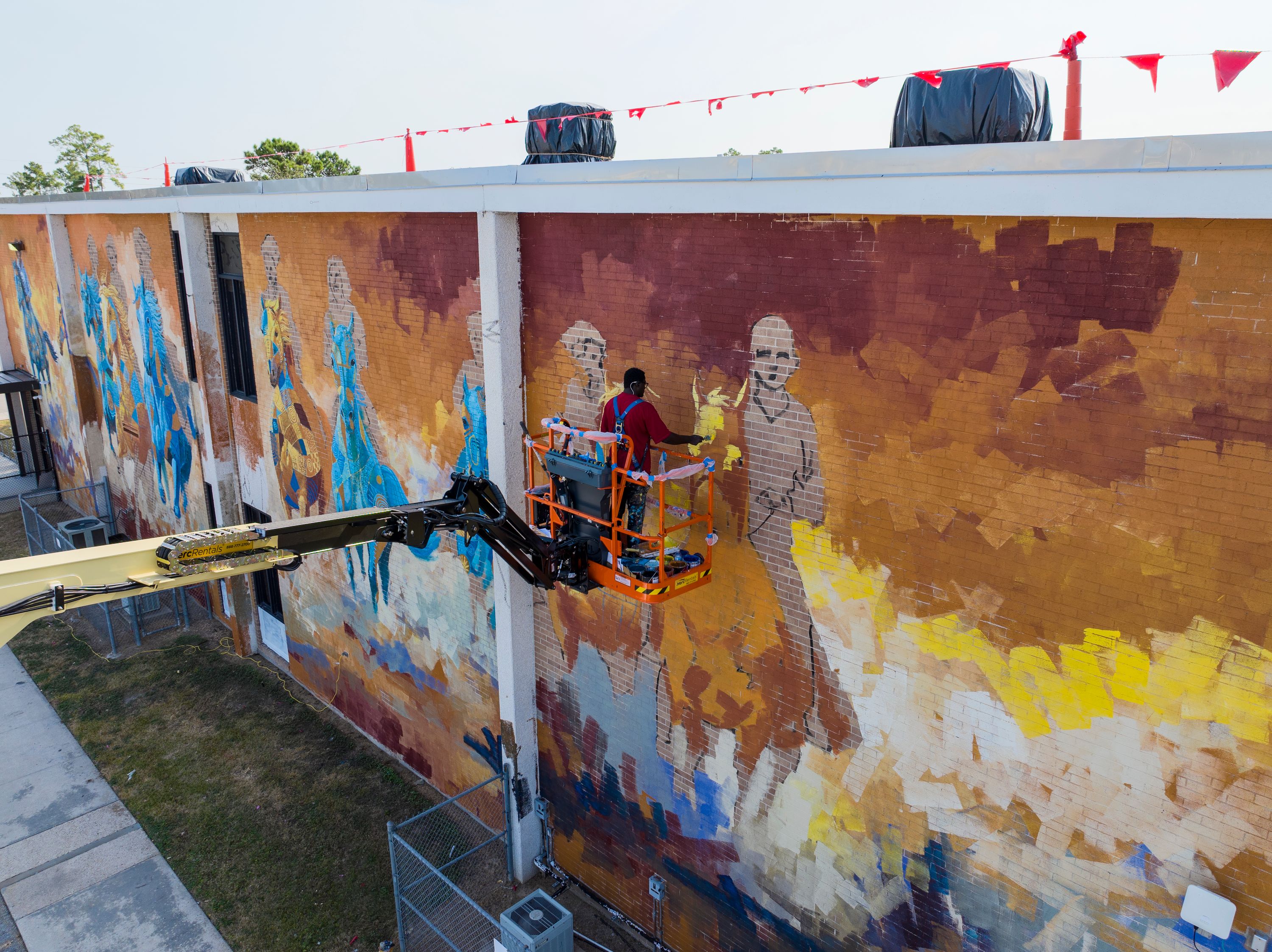 Artist on a boom lift painting the Free Spirits, Golden Hearts mural