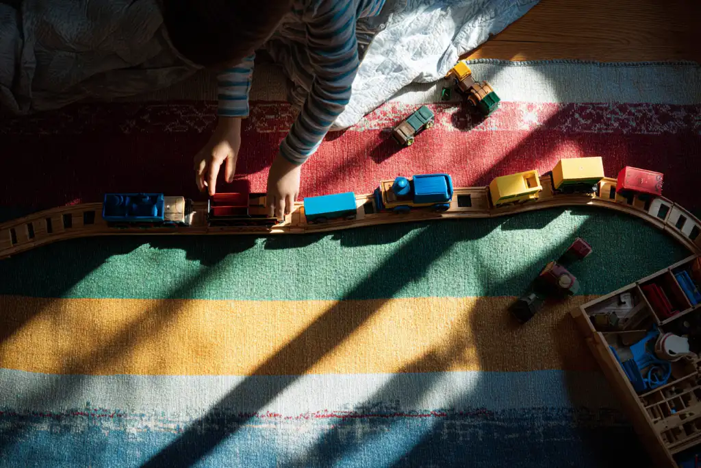 Child playing with wooden toy trains on a striped rug