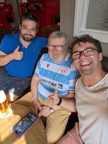 Three people at a table, one holding up a Wrexham shirt