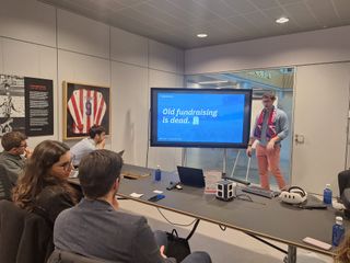 A small audience watching a presentation on a wall screen in a club meeting room