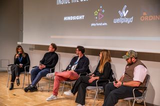 A panel seated on a stage in front of a screen carrying the event sponsors