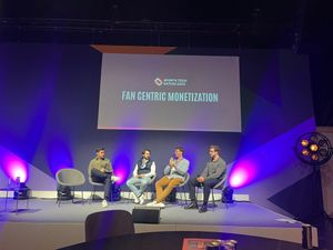Four panellists on a stage lit purple and blue, in front of a screen reading "Fan centric monetization"