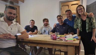 The team standing and sitting around a long wooden table at a culture day, mid-laugh