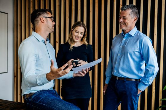 A Trusted Media photograph: three colleagues in discussion against a slatted timber wall