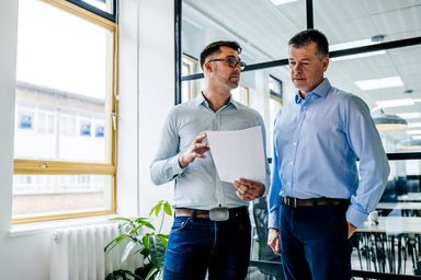 A Trusted Media photograph: two colleagues going through a printed document by a window