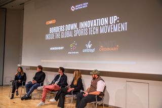 Five people on a stage under the sports tech banner, the moderator at the left with a microphone