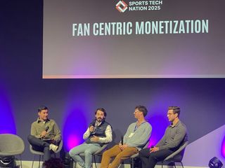 Four speakers seated close together on the Sports Tech Nation stage, screen lit behind