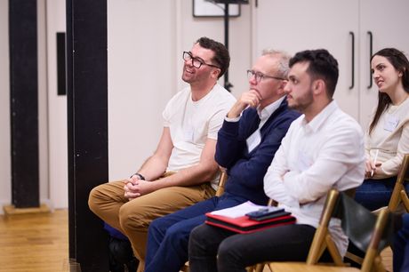 A seated audience in a bright room, listening, some taking notes