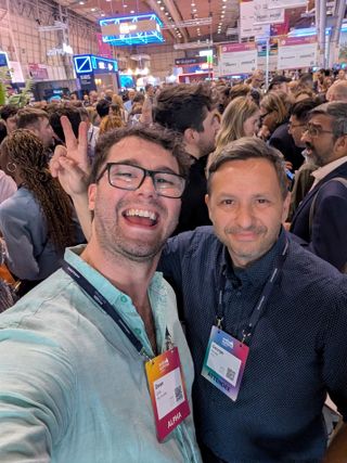 A selfie of two people in a packed conference hall, lanyards on, the crowd filling the room behind