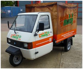 A Snacks Away three-wheeled delivery van parked on a forecourt