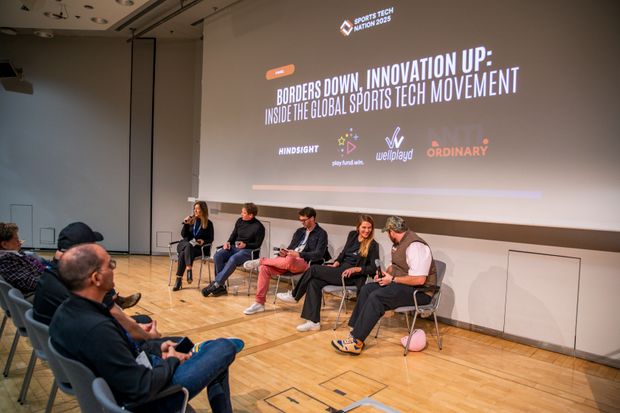 Five panellists seated on a low stage in front of a screen reading "Borders down, innovation up: inside the global sports tech movement", with the audience watching from the front rows
