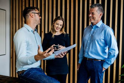 Three colleagues standing around a tablet in a bright office, working through something together