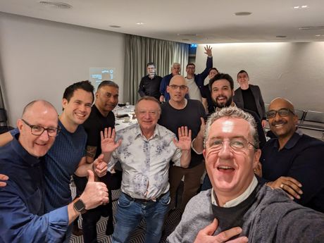A group photograph at the end of a dinner, hands up, everyone laughing