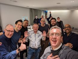 A group photograph at the end of a dinner, hands up, everyone laughing