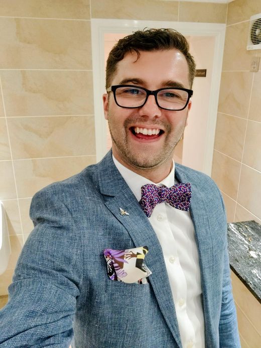 A portrait in a blue suit with a patterned bow tie and pocket square, laughing