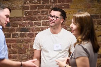 Two people talking beside a brick wall at a networking event, name badges on