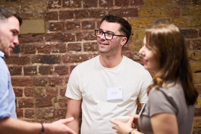 Two people talking beside a brick wall at a networking event, name badges on
